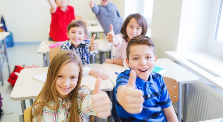 education, elementary school, learning, gesture and people concept - group of school kids sitting in classroom and showing thumbs up