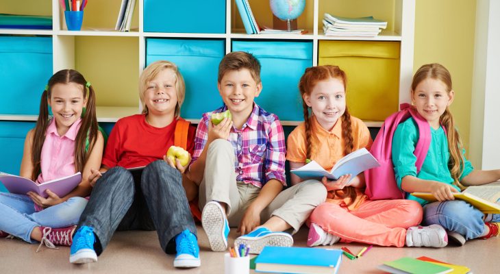 Cute friends sitting on the floor of classroom and doing schoolwork